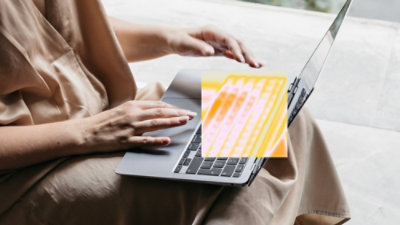 Egy nő kényelmesen ül egy kanapén, és a laptopján dolgozik.