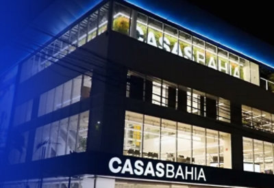 Multi-story building with large glass windows illuminated at night, displaying the name 'CASAS BAHIA' on both the ground and top floors.