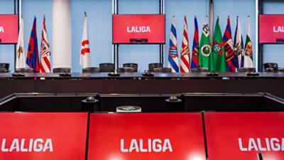 A row of flags in front of a red sign with white text LALIGA.
