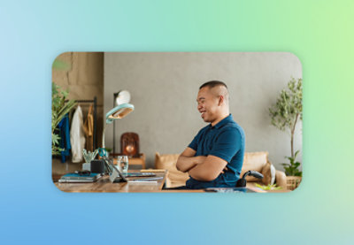 A man in a blue shirt sitting at a desk with his arms crossed.