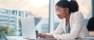 A woman wearing glasses types on a laptop, focused on her work.