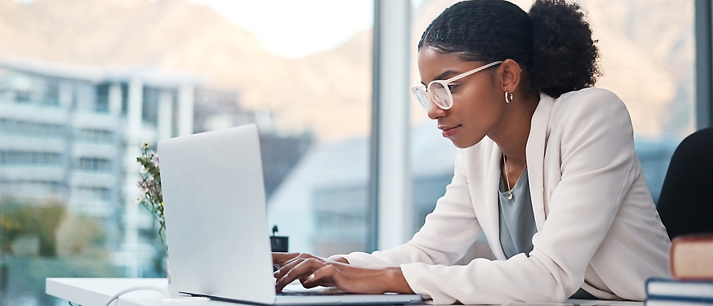 A woman wearing glasses types on a laptop, focused on her work.