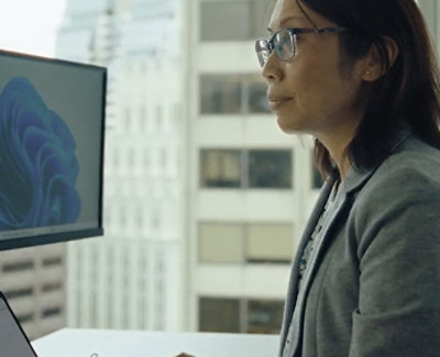 一位戴着眼镜，穿着灰色夹克的女士看着计算机屏幕。