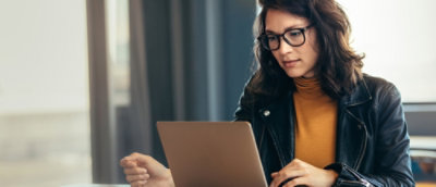 一位戴着眼镜的长发女士正在看笔记本电脑。