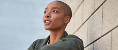 Persona segura con el pelo corto y el anillo de la nariz mirando cuidadosamente a la distancia mientras se inclina contra una pared con textura.