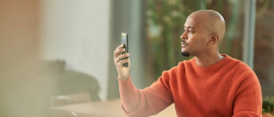 A man wearing an orange shirt taking a selfie with his cell phone.