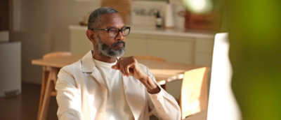 A man with glasses and a beard sitting at a table with his hand on his chin.