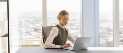デスクに向かって座り、ノート PC を使用している女性。