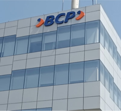 A building with a white wall, a blue sign displaying BCP, and a blue sky with clouds in the background.