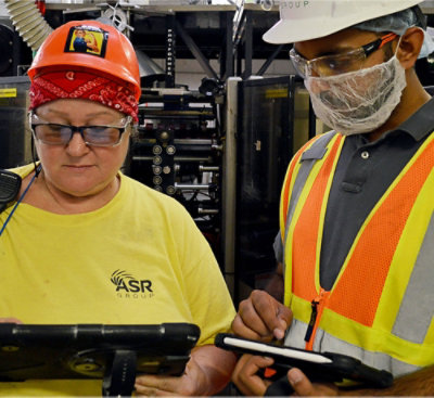 A man in a safety vest and a woman in a hard hat and glasses looking at a tablet with MASR GROUP written in the background.