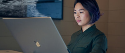 Person working on a silver laptop with a Microsoft logo in a modern indoor setting.