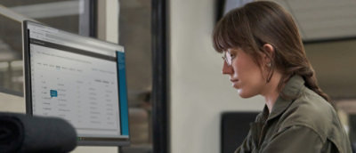 A close-up of a woman with long hair and glasses looking at a computer screen.