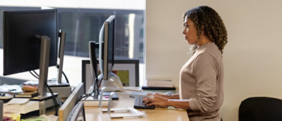 A woman with curly hair works at a standing desk, focused on her computer.