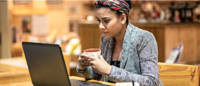 Een vrouw die een kopje koffie vasthoudt terwijl ze een laptop gebruikt.