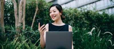 Una donna con un telefono in mano che guarda un portatile.
