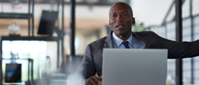 A man in a suit and tie sitting at a desk with a laptop.