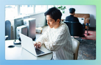 A person wearing a striped shirt is working on a laptop at a table in a well-lit room.