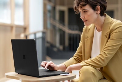 Person in a yellow suit working on a laptop at a small table in a well-lit indoor setting.