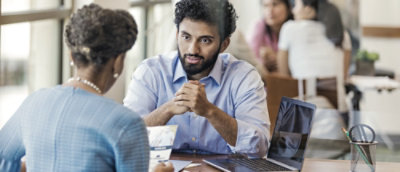 A man and a woman sitting in front of a laptop, discussing.