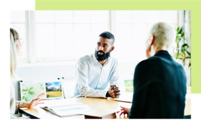Three people are seated at a table in an office setting, engaged in discussion
