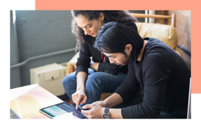 Two people sitting together on a couch, looking at a tablet.