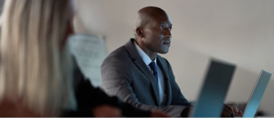 A man in a grey blazer sits at a desk with his laptop