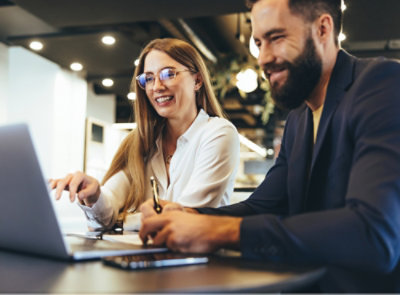 Two people sitting at a table with laptops, engaged in a discussion