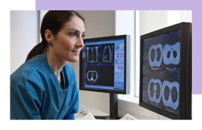 A woman in blue scrubs looking at computer screens.