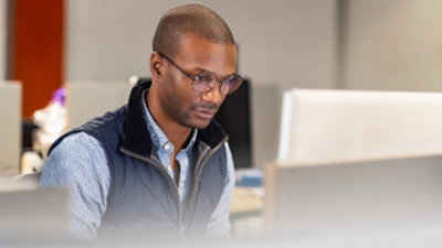 A man wearing glasses and looking down at a computer.