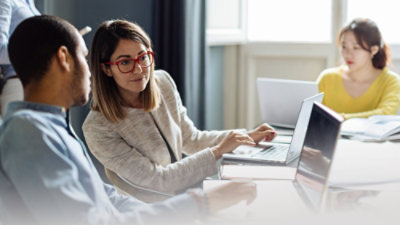 A man and woman sitting in a room looking at a laptop.