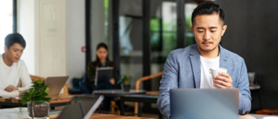 A person in a suit holding a cup and looking at a laptop.