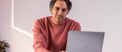 A man wearing glasses sitting while looking at a laptop.