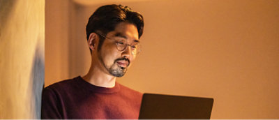 En mann med briller og en rød skjorte, som holder en bærbar datamaskin.