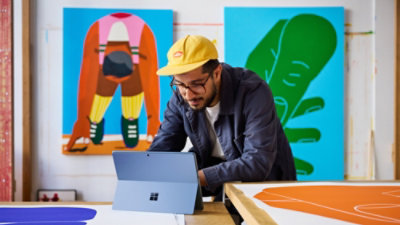 A person wearing a yellow hat looking at a laptop.