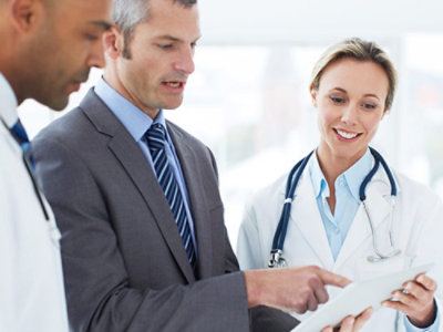 Three professionals, two doctors and a businessman, discuss information on a tablet.