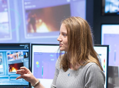 Person gesturing while seated in front of multiple monitors displaying thermal and fire-related images.
