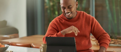 A man in orange hoodie sitting and looking at a tab.