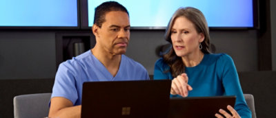 A man and woman looking at a laptop on a desk.