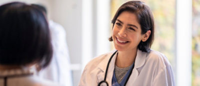 A smiling woman in a white coat with a stethoscope around her neck.