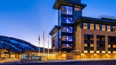 Modern hospital building at dusk with illuminated windows and a tall glass tower.