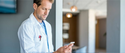 A man wearing a white coat looking at a cellphone.