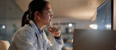 A focused doctor in a lab coat and glasses examines brain scans on a computer screen.