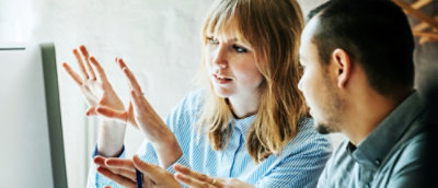 Two people engaged in discussion at a desk, focused on a computer screen.