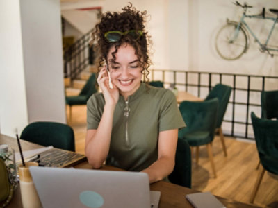 A woman talking on a cell phone while using a laptop.