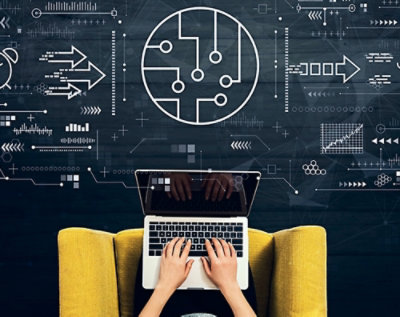 En person set fra oven, der bruger en bærbar computer med digital grafik relateret til teknologi og innovation projiceret på væggen foran.