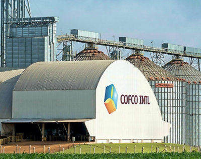 En stor hvid bygning med et COFCO INTL PE-logo og en grøn mark i baggrunden.