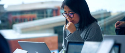 En kvinde i en grøn top fokuserer på sin bærbare skærm, delvist indrammet af et blåt grafisk element