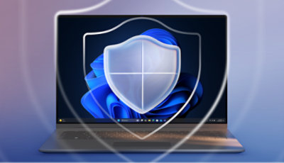 Laptop displaying Windows 11 with a semi-transparent shield icon overlay on a purple-blue gradient background.
