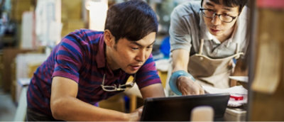 A man wearing glasses and an apron looking down at a laptop.