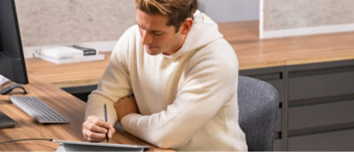 A person holding a pen and writing on a tablet.
